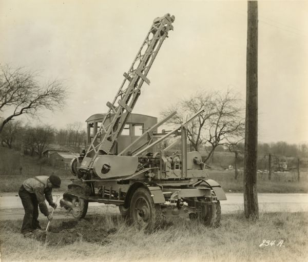 A man uses a post hole digger manufactured by the Winther Motors Inc., factory.