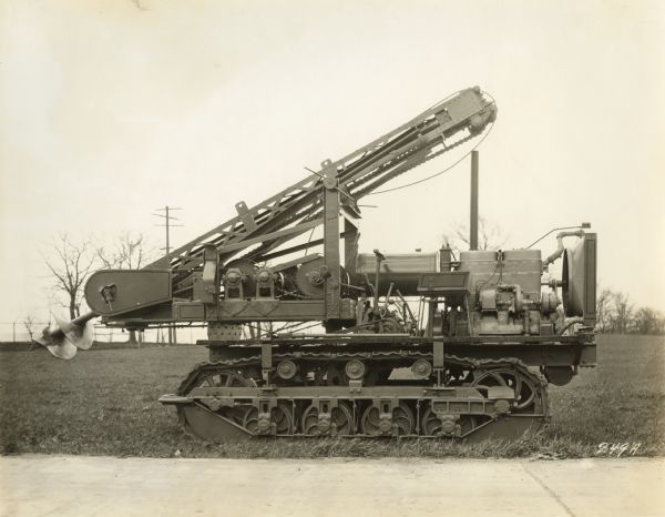 Side view of a posthole digger manufactured by the Winther Motors Inc., factory mounted on a Caterpillar tractor.