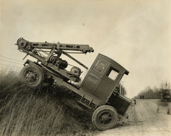 A truck with a posthole digger mounted on back on the side of the road, manufactured by Winther Motor and Truck Company.