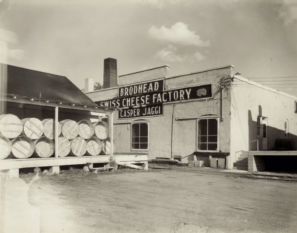 Exterior of the Brodhead Cheese Factory purchased in 1904/5 by Casper Jaggi.   The business shipped cheese in barrels, which were at first stored in the open, via railroad to Charlie Zucher of Chicago.  Englebritzen mural, extended can track, ramp/boiler room, and whey tanks were added later.
