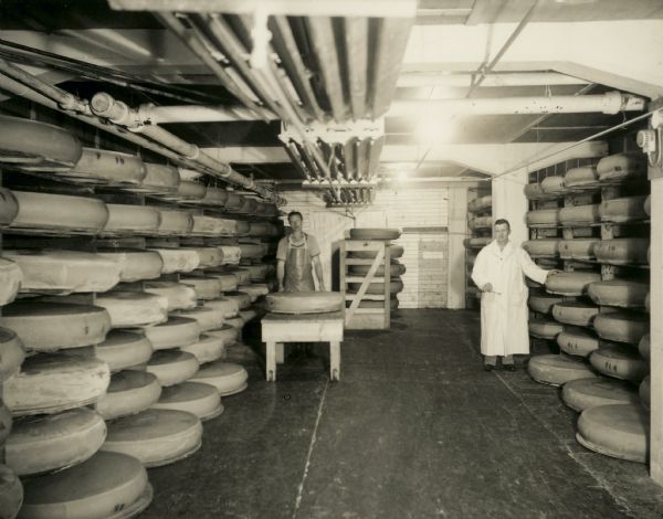 Two men stand with cheese in the cooling room.