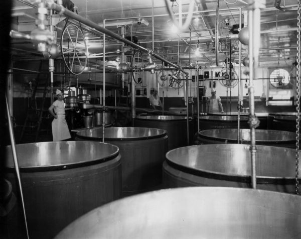 Two men in the Brodhead Cheese Factory in a room that contains a separator, vats and stirrers.