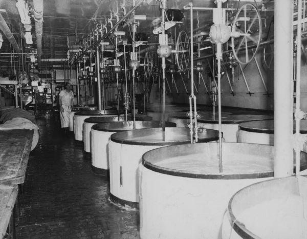 Interior of the Brodhead Cheese Factory with a man by a vat.