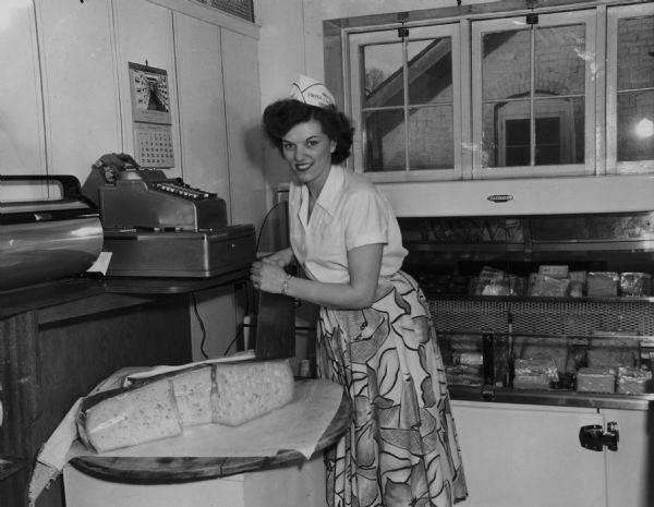 June Swensen at a register cutting a wheel of cheese.