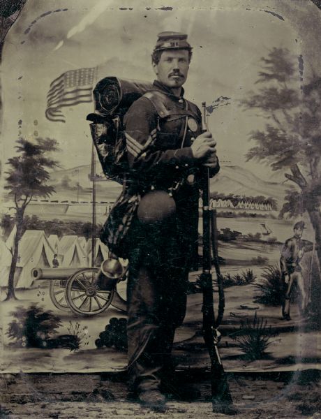 Full-length portrait in front of a painted backdrop of an unidentified Civil War soldier standing and holding a rifle.