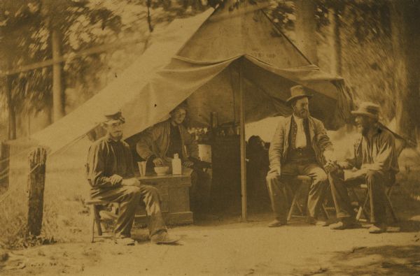 A surgeon examines a patient at the steward's quarters.  Joseph W. Curtis, hospital steward, is inside the tent, seated on a medicine chest.