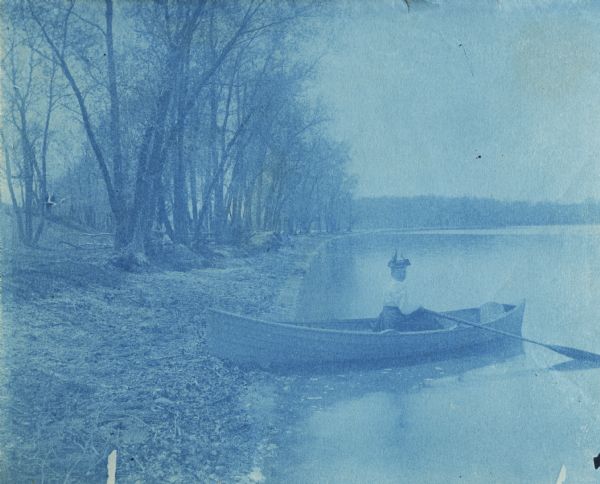 Cyanotype image of a woman in a rowboat on the shore of the University Willow Walk, near picnic point.