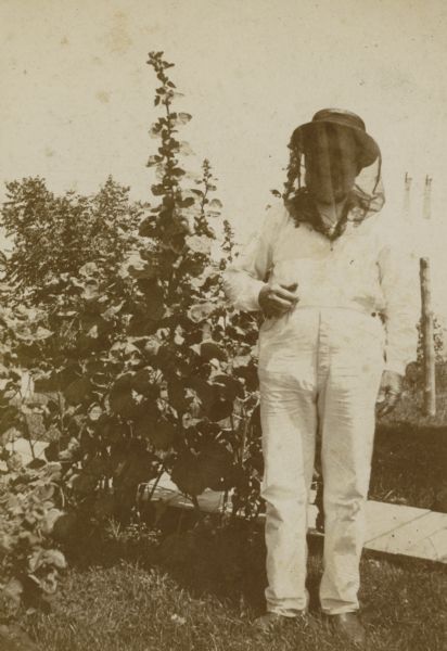 A beekeeper stands outside in protective clothing.