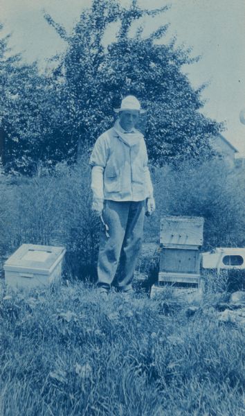 A cyanotype postcard of a bee farmer working in his field.