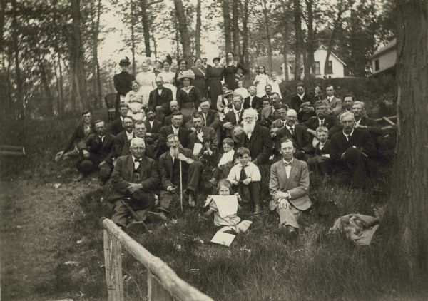 A group portrait of Iowa and Wisconsin beekeepers in the woods with houses in the background.