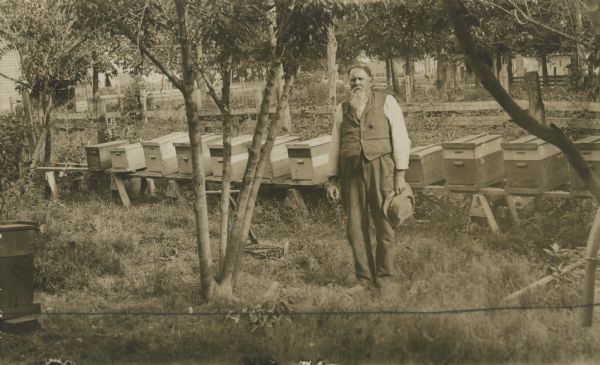 A man stands near rows of beehives sitting on boards and saw horses.