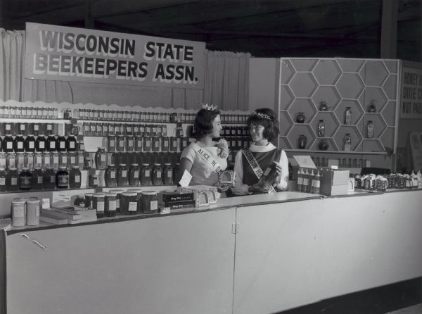 Alice in Dairyland and the Wisconsin Honey Queen standing at a Wisconsin State Beekeepers Association stand, possibly at the Wisconsin State Fair.