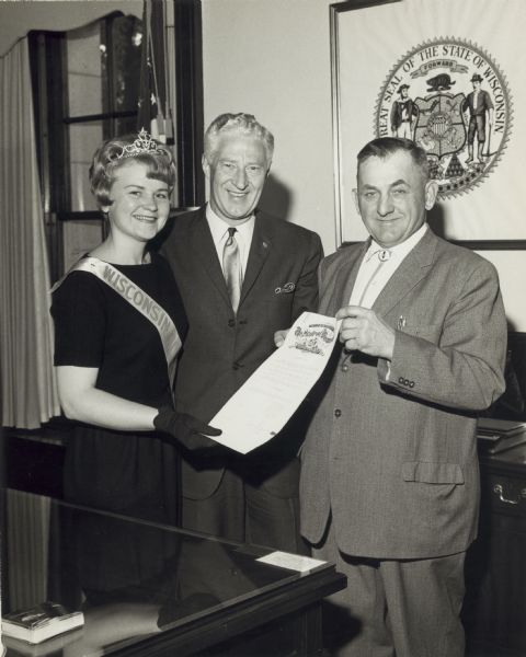 Wisconsin Honey Queen holding a document with the 1966 Wisconsin Honey Producers Association President B. E. Gustner, with Governor Warren Knowles standing in the middle.