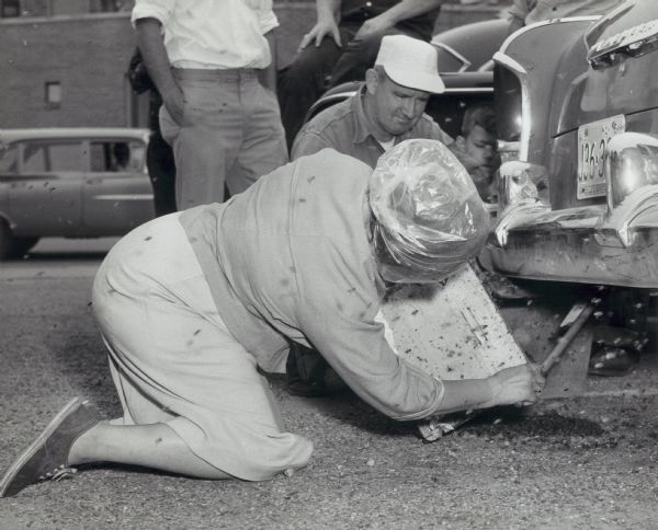 A woman removes a swarm of bees from the bumper and tail pipe of a car.