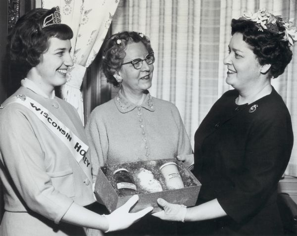 Mrs. Wiley, wife of Senator Alexander Wiley (R., Chippewa Falls, Wisconsin), presented with a box of honey by the Wisconsin Honey Queen. Next to her is her chaperon Mrs. Bogan.