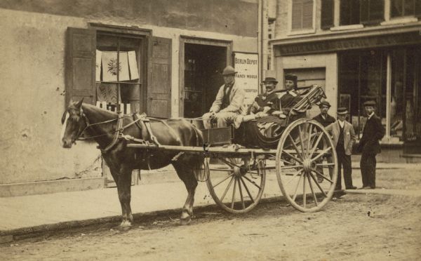 A carte-de-visite of a man and woman sitting in a buggy behind the driver. Three men are standing behind the buggy. Back of card reads: "Caliche, Quebec".
