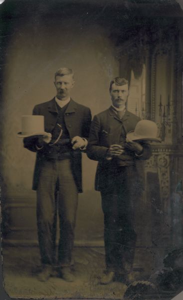 Tintype (ferrotype) of two men in a studio holding white hats.