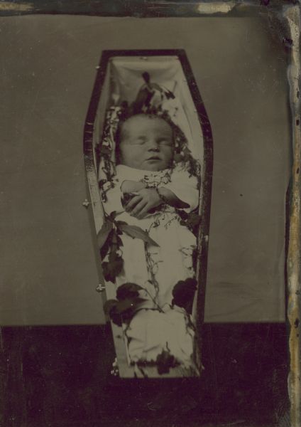 Tintype (ferrotype) of a dead baby in casket, covered with roses.