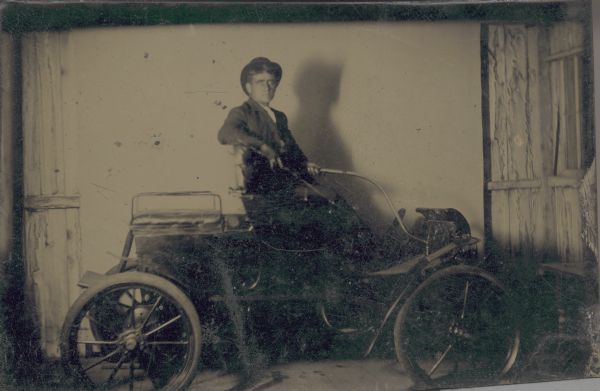 Tintype (ferrotype) of a man seitting in an early automobile.