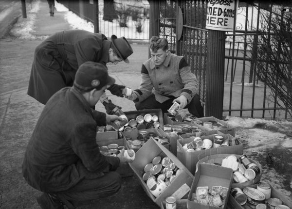 Harnischfeger workers aren't on strike but they do their bit every week to help those who are.  This picture was taken at the end of a regular Wednesday morning plant-gate collection for canned goods.  As you can see the contributors gave generously--and if they forgot their can of food, they dropped some change in the collection box.  Local 1114, USA [United Steelworkers of America], members at that plant have pledged to continue the weekly food and fund collections for the duration of the strikes. Wisconsin CIO News.
