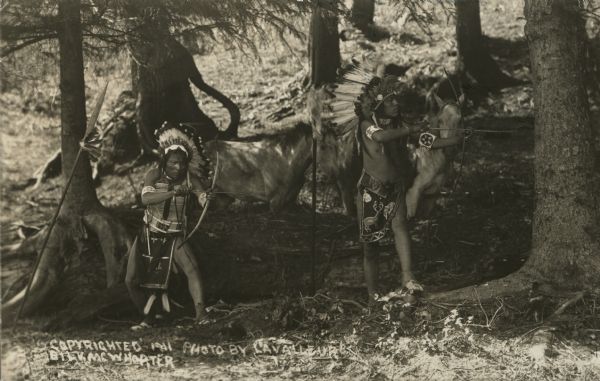 Two American Indians with their horses, posing with their bows.