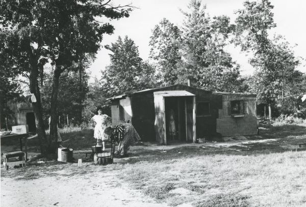 Two Native American women in front of a small house doing yard or house work.