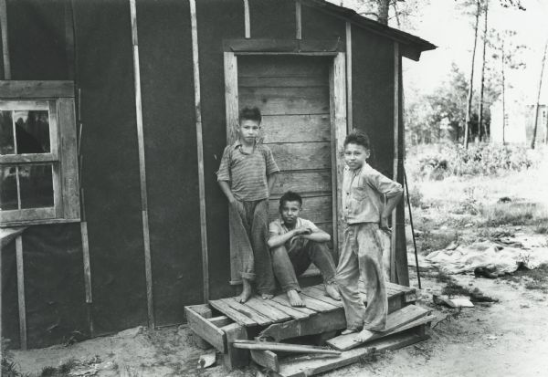 A group of three Native American boys standing in front of a door.