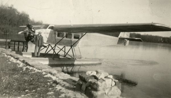 A pontoon airplane floating on a lake with a man next to it.