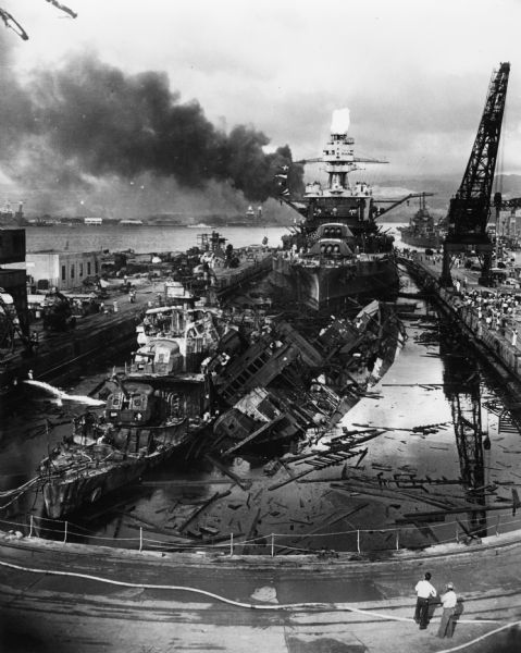 The remains of the USS <i>Cassin</i> and the USS <i>Downes</i> floating in front of the USS <i>Pennsylvania</i> in dock at Pearl Harbor.  On the left is the destroyer USS <i>Downes</i> that was ravaged by torpedoes, bombs, and the explosion of its own munitions.  On the right is the destroyer USS <i>Cassin</i> that was severely damaged by bombs and torpedoes which caused it to roll off of its blocks into the USS <i>Downes</i> while capsizing.  Behind the two is the battleship USS <i>Pennsylvania</i> which was only lightly damaged.