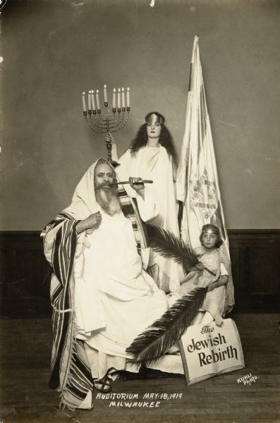 A Jewish man, woman, and child dressed as Old Testament characters standing in front of an Israeli flag.