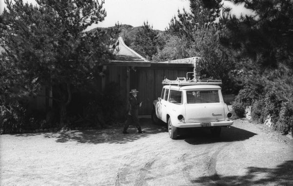 Ansel Adams at his home in Carmel walks toward his International Travelall with camera platform mounted on top.