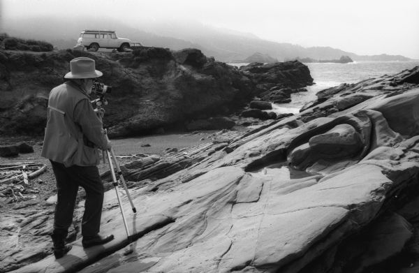 Ansel Adams with a Hasselblad camera mounted on a tripod prepares to make a photograph at Point Lobos. His International Travelall is in the background.