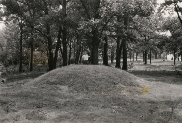A man poses behind a conical Native American burial mound near the west end of Picnic Point on the University of Wisconsin-Madison campus.