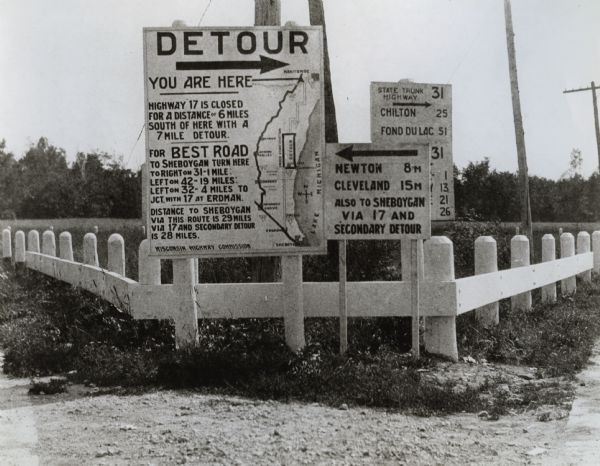 Detour sign posted by the Wisconsin Highway Commission, the predecessor of the Department of Transportation, in Manitowoc showing a confusing detour route to Sheboygan.  In 1917 the Highway Commission adopted a standard signage format and numbering system.  This sign identifies the detour route by number so the photograph must postdate 1917, although its informality suggests that it must have been shortly after.