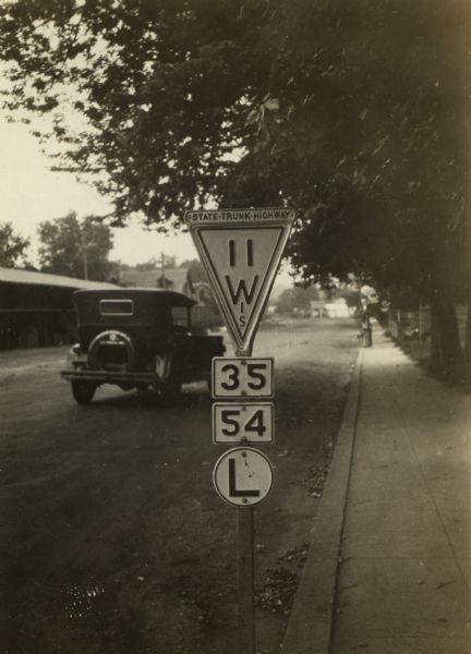 Wisconsin State Highway sign along STH 11 near Galesville, one of a whole new vocabulary of signage created for automobile traffic. The inverted triangle was used as a standard state highway sign at least through the 1920s in cities and villages where no post was available.  A shield shaped sign similar to that adopted by the federal government was used when a pole was available. The lower numbers indicated that state highways 35 and 54 could be reached by a left turn ahead. In 1933 State Highway 11 became US Highway 14.