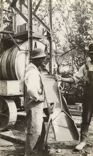 Two African American men unloading the cement chute during paving of Janesville Plank Road.