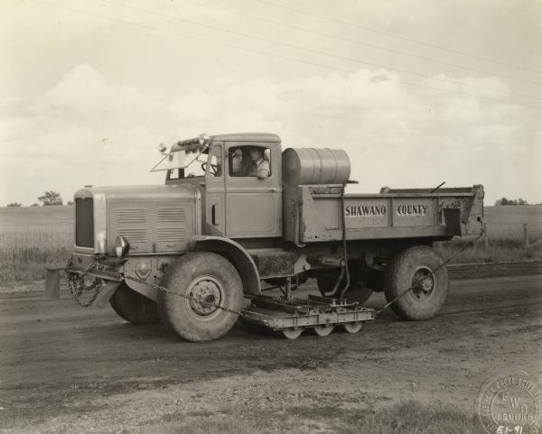 Dump truck manufactured by the Four Wheel Drive Co. of Clintonville and owned by Shawano County.  The truck is equipped for rolling and dressing unpaved roads.  This image was used for publicity purposes by the Four Wheel Drive Company.