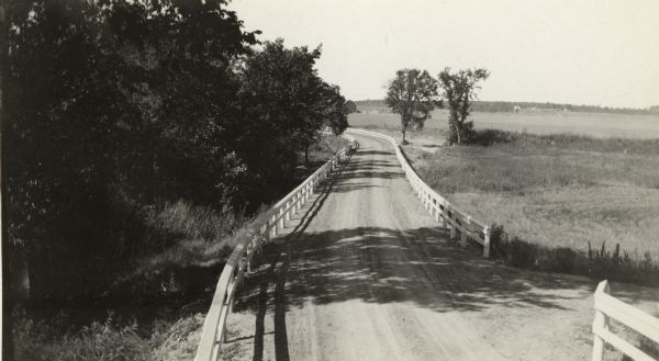 Amery Road near New Richmond.  The photograph was taken by the Wisconsin Good Roads Association probably as an illustration of the kind of improved roads that the organization advocated.  The photograph also appeared in the Highway Commission's annual report in 1918 with a comment on the fill well protected by a guard rail.