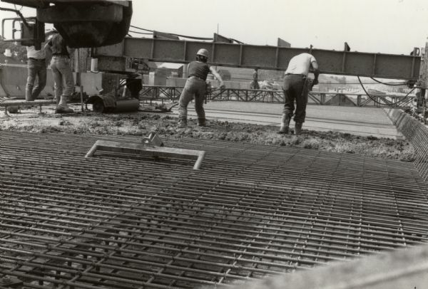Concrete pour during the construction of an unidentified Wisconsin highway.  The crew for this job includes a woman.