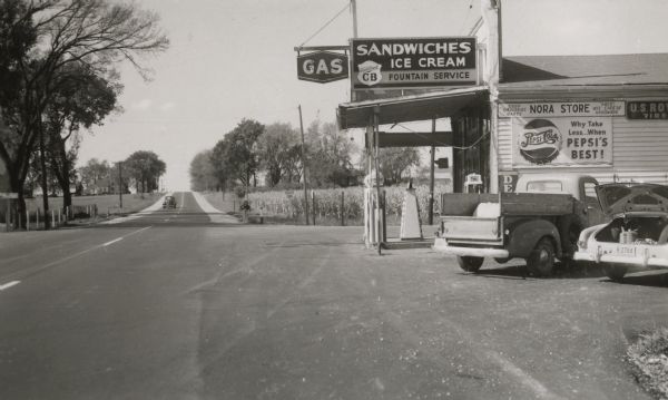 Corner store at Nora on Highway 12 & 18 near Cambridge which sold not only gasoline but also ice cream and soda pop for weary travelers. The Highway Department employees who took this photo to document the bituminous concrete resurfacing noted that the driveway to the store had been illegally blacktopped.