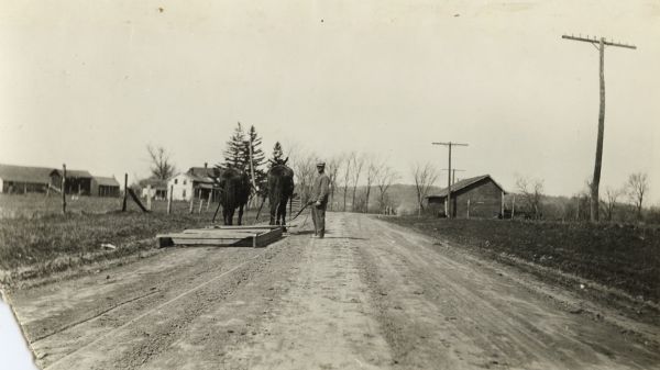 Patrolman leveling the surface of State Highway 33 in the town of Excelsior in Sauk County using a team of horses and a wooden grader.  Patrolmen were instructed to begin grading after a rain storm in the center of the road.  The original caption indicates that the surface seen in the photograph was achieved after two round trips.