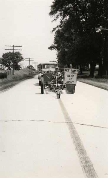 A highway employee rides the machine which painted the center line of paved highways.