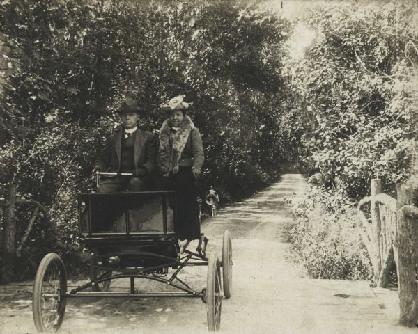 Mr. and Mrs. Albert G. Zimmerman in their locomobile steamer in 1902.  Zimmerman purchased the car in 1901 and claimed it was the first permanent automobile in the capital city. "Prof. Wood had one like it for experimental purposes," he wrote on the back of the photograph,"a month or two before, but he took it away with him to Baltimore that summer." The Zimmermans are seen on the Shorewood rustic bridge, a picturesque highlight of Lake Mendota Drive. The Park and Pleasure Drive created the drive a decade earlier for scenic excursions in horse-drawn vehicles. To prevent trouble with the horses, early autos and carriages used the pleasure drive on different days.