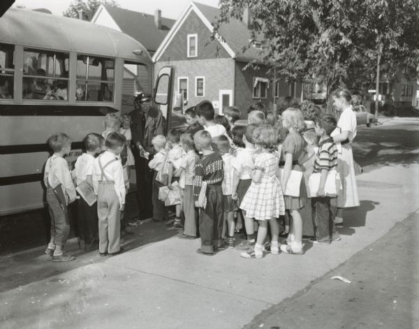A group of elementary school students getting ready to board a bus, while the driver is handing out ice cream as they board.