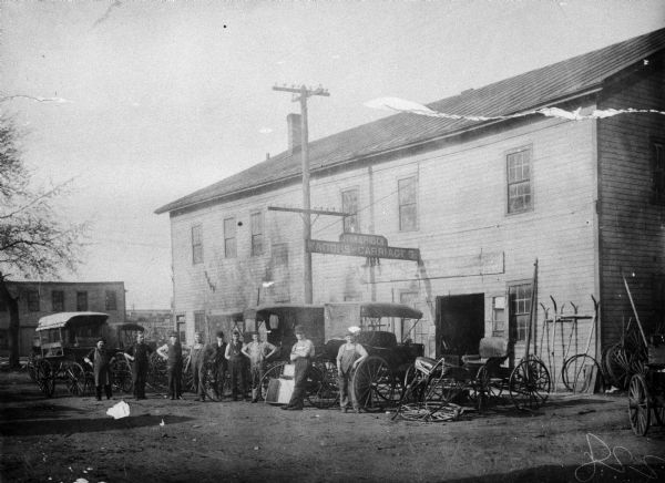 Exterior view of the wagon shop of John B. Pirsch of Kenosha whose father, Nicholas Pirsch, had begun building buggies and wagons in 1857. Several men pose in front of the building.