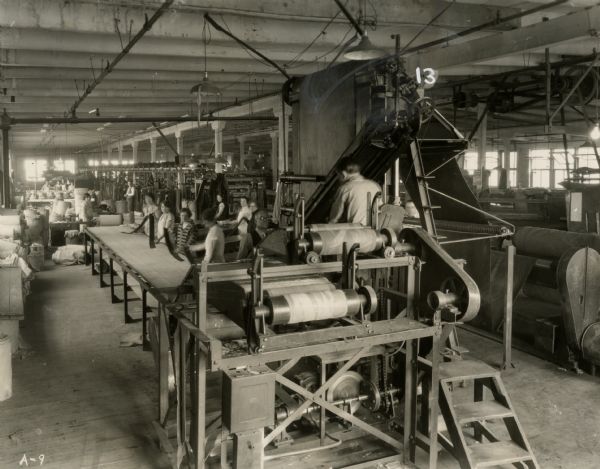 Cutting machine at the Ajax Rubber Company of Racine.  In the foreground the cutting machine automatically cuts frictioned fabric on the bias, then women workers along the conveyor lap the ends and the coated fabric is wound on rolls or made into pockets to be used for the tire building.