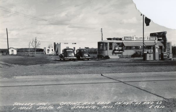 The Trolley Inn, diner, overnight cabins, and gas pumps, located on state highways 53 & 63, one mile south of Spooner.  The juxtaposition of the former trolley car and the parked cars is an ironic representation of the way in which automobiles brought about the end of street railroads for urban transportation.