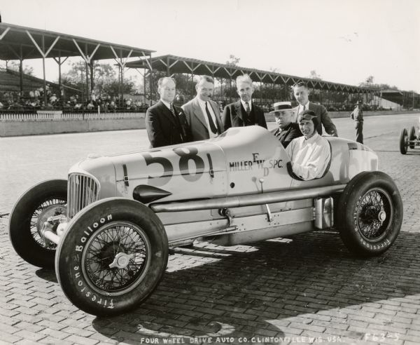 The Miller Engine-Four Wheel Drive Special and executives of the Four Wheel Drive Company of Clintonville at the Indianapolis Speedway in 1932.  FWD personnel in the photograph who assisted in the development of the race vehicle include H.B. Dodge, chief engineer (standing on the left), Frank Gause, FWD secretary (third from the left) and Walter Olen, FWD president who is seated in the car next to the driver, Bob McDonogh, a veteran Indy race car driver.  Also part of the group in the backrow (second from the left, with cigar) is the famous race driver Barney Oldfield who was the FWD race team manager.