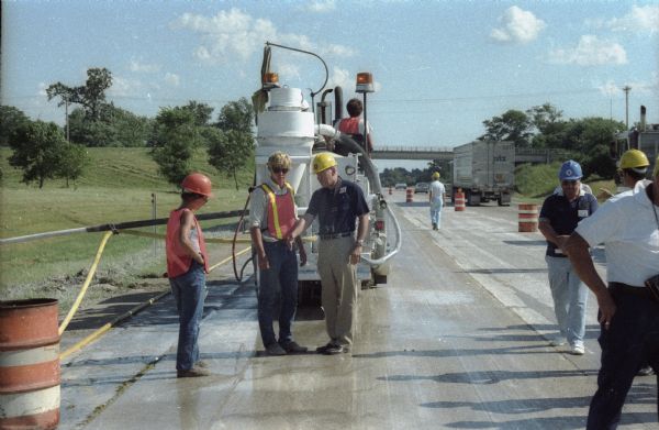 A construction superintendent talks with two highway construction workers (one of whom is a woman), during a resurfacing operation on interstate highway I90&94.  Although undated on the original print, this operation probably dates to the mid-1980s.