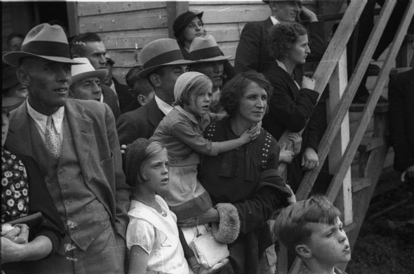 Audience at the Wisconsin State Fair, probably watching the children's pony races.  One mother holds her daughter in her arms so that she can see better.